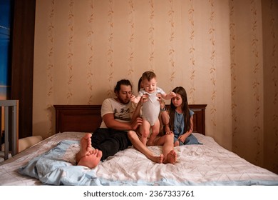 Long range shot of beautiful family on the bed in the morning in the sun from window. Tactile hugs of mother, father, daughter, son. Family weekend, relaxation at home. General view of family bedroom - Powered by Shutterstock