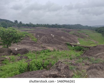 Long Range View Of A Landscape With Rocks And Rainy Clouds Filled With Grass And Trees