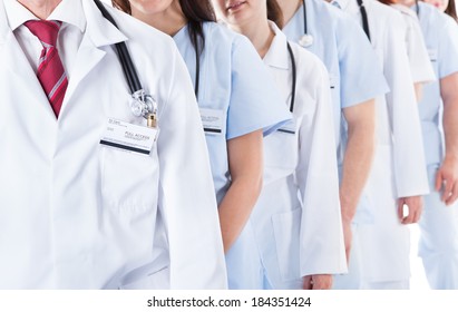 Long receding line or queue of smiling doctors and nurses in white uniforms wearing stethoscopes around their necks isolated on white