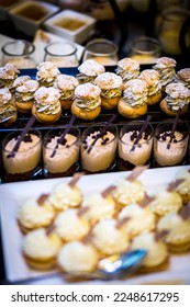 Long rectangle shaped plates filled with various types of sweets and cakes on a wooden table filled with food