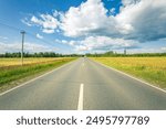 A long road with a clear blue sky and a few clouds. The road is empty and there are no cars on it