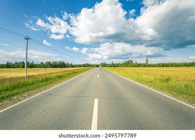 A long road with a clear blue sky and a few clouds. The road is empty and there are no cars on it - Powered by Shutterstock