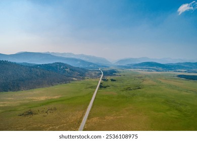 A long road stretches through expansive green plains towards distant mountains under a clear blue sky. The serene landscape offers a sense of peace and endless possibilities. - Powered by Shutterstock