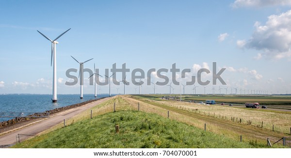 Long row of windmills in the water next to\
the busy road. Lots of cars and trucks.\
