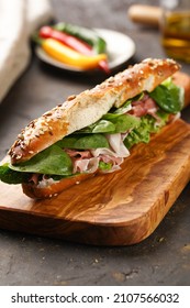 Long Sandwich In Brown Lye Bread Sticks Garnished With Oats , Pork Slices Prosciutto, Hard Cheese Gouda And Fresh Greens On Wooden Boards