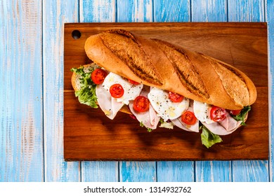 Long Sandwich On Cutting Board On Wooden Table