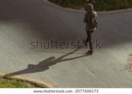 Long shadow of a girl on a paved footpath in the bright morning sun. Moving forward, play of light and shadow