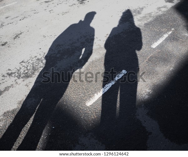 Long shadow of man and woman on asphalt road\
with dividing line\
outdoors.
