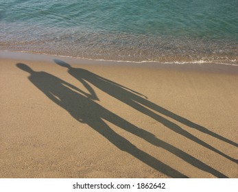 Long shadow of young couple holding hands cast on beach sand - Powered by Shutterstock