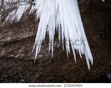 Long sharp icicles hanging from limestone rock overhang at Šikľavá skala near Matejovce nad Hornádom, Slovakia, forming a frozen waterfall in winter landscape.
