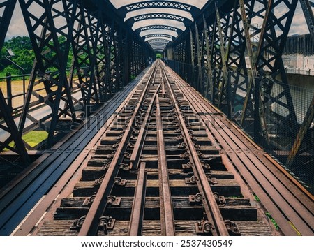 A long shot down the center of a historic Victoria Bridge in Kuala Kangsar,Perak.A railway bridge with multiple tracks and a wooden walkway,spans a river valley with lush green trees in the background