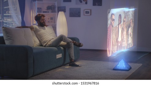 Long shot of man watching holographic TV at night
