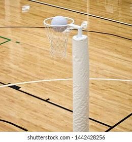 A Long Shot Showing A Netball Goal With A Netball Ball Entering The Metal Ring. Glossy Wooden Floorboards Of An Indoor Netball Court Serve As The Background.