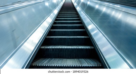 Long And Steep Escalators From The Bottom Looking Upwards As A Person Is About To Travel From The Ground Level Up To The Next Floor.