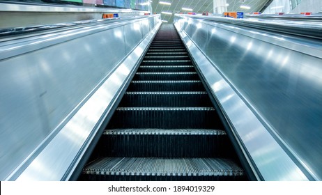 Long And Steep Escalators From The Bottom Looking Upwards As A Person Is About To Travel From The Ground Level Up To The Next Floor.