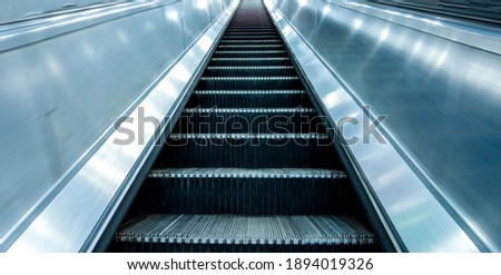 Long and steep escalators from the bottom looking upwards as a person is about to travel from the ground level up to the next floor.