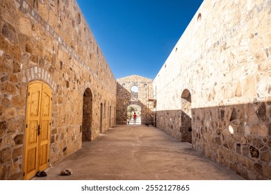 Long stone corridor with arches and wooden doors, scaffolding in the background, and clear blue sky above. - Powered by Shutterstock