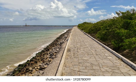 A Long Stone Walkway Next To The Wavy Ocean Under The Cloudy Blue Sky