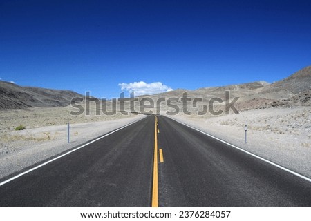 A long, straight highway winding its way through a vast desert landscape under a blue sky.