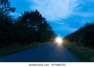 A Long Straight Road, With Car Headlights In The Distance. On A Summers Evening. UK.