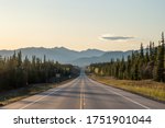 Long straight road heading towards large mountains in Yukon Territory, northern Canada in the spring time on the Alaska Highway. 