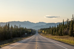 Long Straight Road Heading Towards Large Mountains In Yukon Territory, Northern Canada In The Spring Time On The Alaska Highway. 