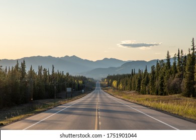 Long straight road heading towards large mountains in Yukon Territory, northern Canada in the spring time on the Alaska Highway. 