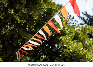 A long string of flags with red and white stripes. The flags are hanging from a tree. The flags are of different sizes and colors. The scene is bright and cheerful