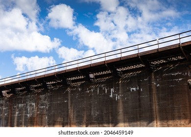 Long And Tall Industrial Concrete Wall With Rusted Metal Catwalk Before Blue Sky With Clouds, Horizontal Aspect