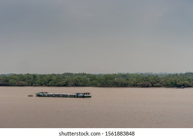 Long Tau River, Vietnam - March 12, 2019: Long Segmented Hull River Barge Sails On Brown Water And Lies Deep. Green Belt Separates From Light Blue Sky.