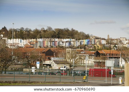 Long terrace of colored houses in Bristol UK, with vehicles, trees, parked cars and a busy main road