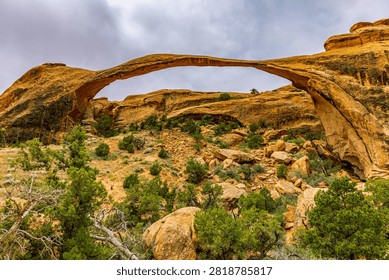 The long, thin span of Landscape Arch stretches above a rocky desert slope in Devils Garden, Arches National Park.
