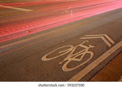 Long Time Exposure Of Bicycle Lane Symbol On Road At Night With Car Tail Lights Streaking By Above