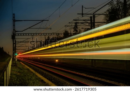 Long time exposure at night of a train passing by in a rural area.  Ahead a red and a green signal light. Light trails, being reflected off the surface of the rails.