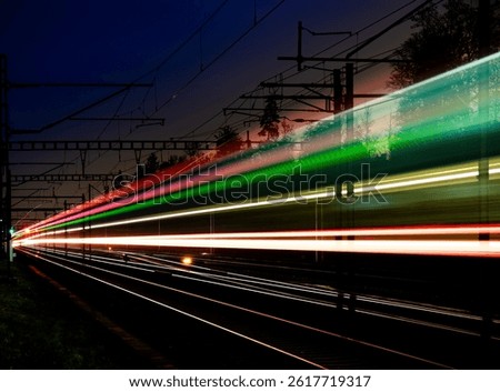 Long time exposure at night of a train passing by in a rural area. Red, blue, pink, green and white light trails, being reflected of the surface off the rails. Dark blue sky.