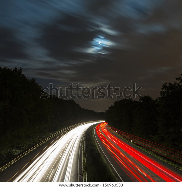 long time exposure on a highway with car light trails\
and moon in the sky