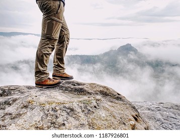 Long Tired Male Legs In Hiking Trousers Stay For Moment On Peak Of Rock Above Valley.