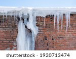 Long transparent icicles hang from the roof. The icy gutter is like a giant icicle. Icicles falling danger concept.