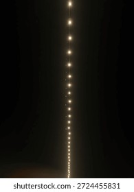 A long, vertical line of glowing string lights descends against a deep, dark night sky, creating a magical, elegant atmosphere