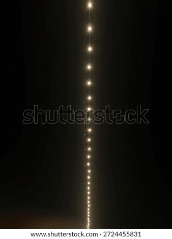 A long, vertical line of glowing string lights descends against a deep, dark night sky, creating a magical, elegant atmosphere