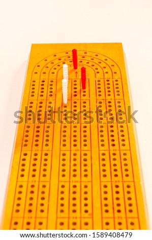 Long view of a cribbage board with white and red pegs at the finish point on a white background.