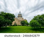 Long view of the Illinois State Capitol Building in Springfield, IL, USA. Cloudy overcast skies overhead. Springtime scene with a lush green lawn and full trees.