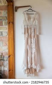 A Long White And Pink Bridesmaid Dress With Embroidery And Sequins Is On A Hanger On The Wall