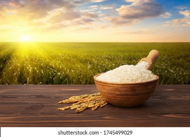 Long White Rice In Bowl With Ears On Table Against The Green Agricultural Field