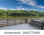 a long winding boardwalk along the Chattahoochee river with a wooden rail, still river water, green trees with blue sky and clouds at Roswell Riverwalk Boardwalk in Roswell Georgia