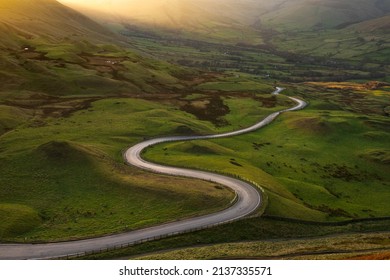 Long winding road in British rural countryside leading off into distance. Peak District, UK.