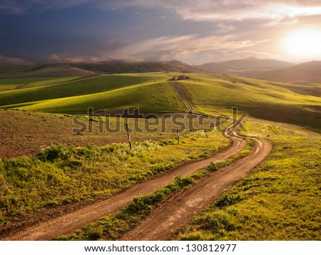 a long and winding rural path crosses the hills at the sunset