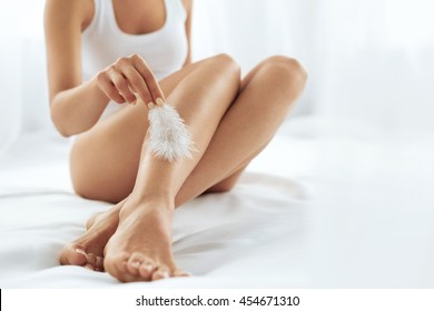 Long Woman Legs With Beautiful Smooth Skin. Closeup Of Female Hand Touching Perfect Hairless Soft And Silky Skin With White Feather. Hair Removal And Epilation, Beauty Body Care Concepts