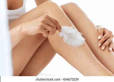 Long Woman Legs With Beautiful Smooth Skin. Closeup Of Female Hand Touching Perfect Hairless Soft And Silky Skin With White Feather. Hair Removal And Epilation, Beauty Body Care Concepts