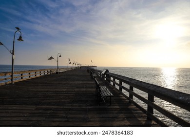 a long wooden pier with American flags and curved light posts along the pier with people walking along the pier and blue sky and clouds at sunset at Surfers Point at Seaside Park in Ventura California - Powered by Shutterstock